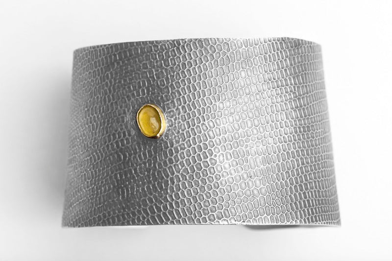 Flat-lay of the Reptilia Maxima silver cuff with yellow aragonite cabochon and snake-scale texture.